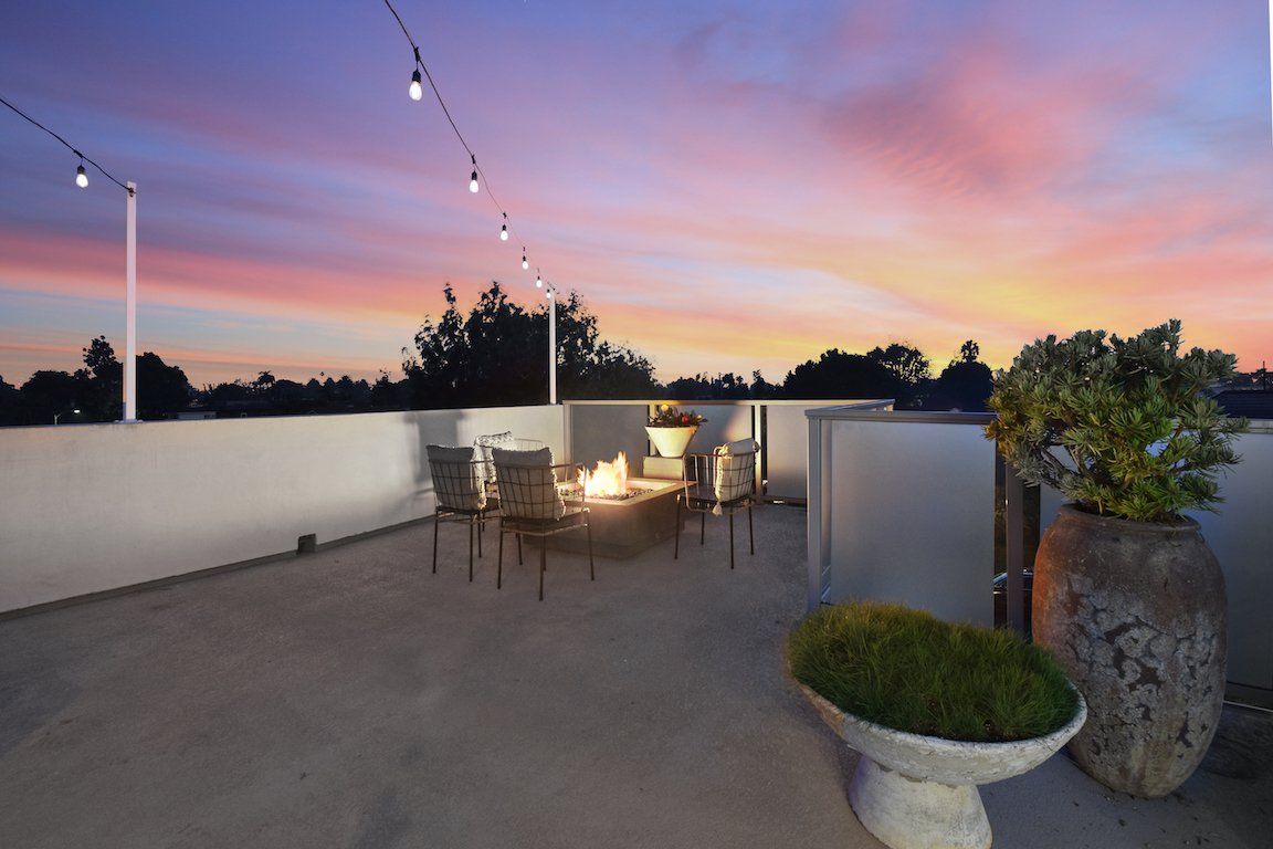 A rooftop deck with a fire pit and chairs at sunset