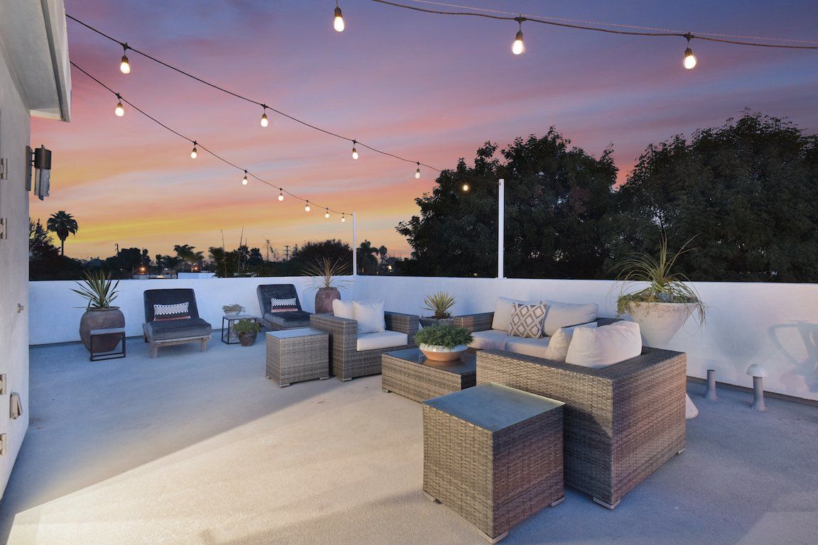 A patio with wicker furniture and a string of lights at sunset