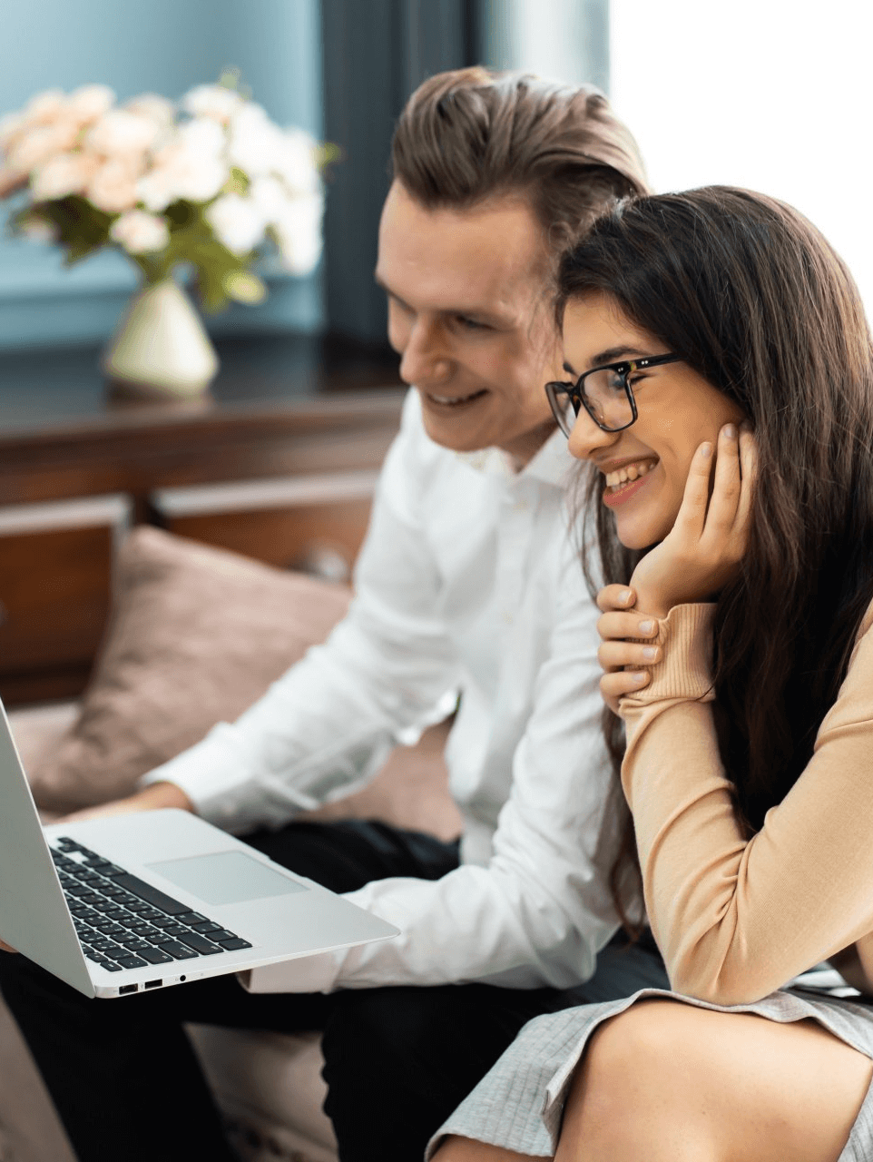 A man and a woman are sitting on a couch looking at a laptop.