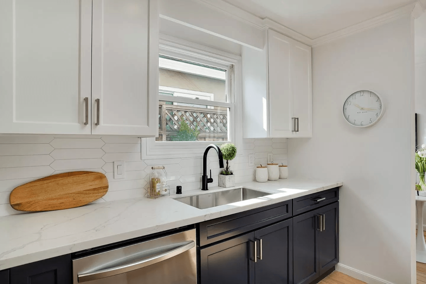 A kitchen with black cabinets , stainless steel appliances , a sink and a window.