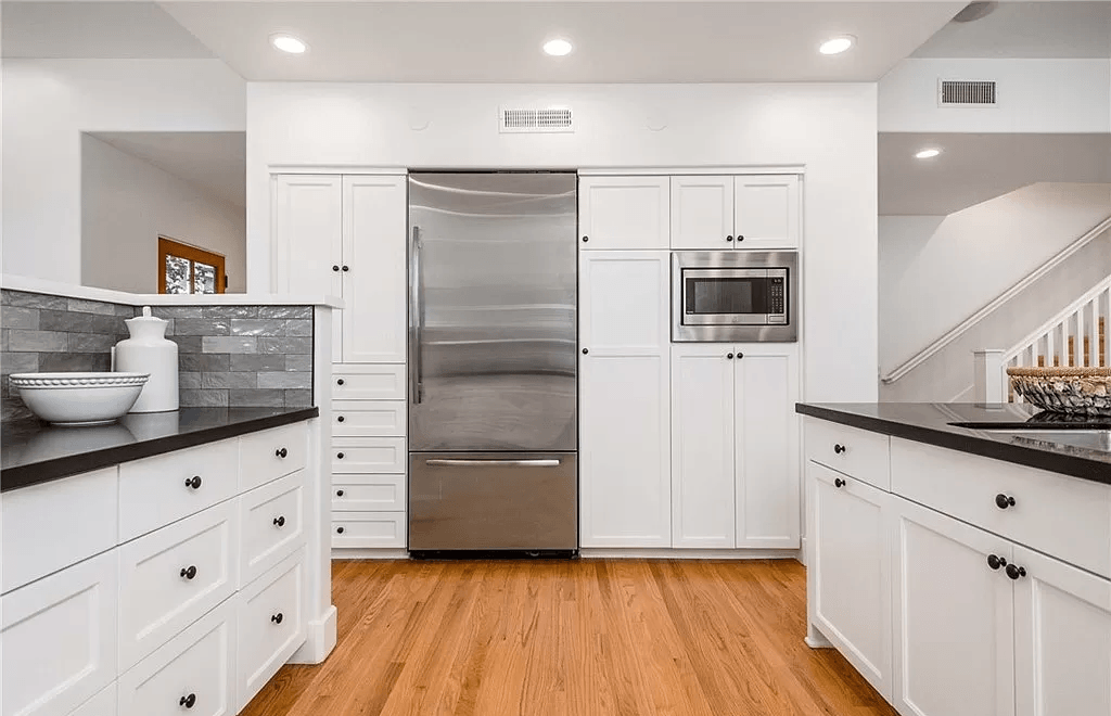 A kitchen with white cabinets , stainless steel appliances and hardwood floors.