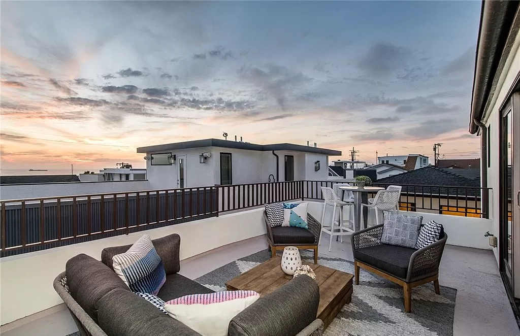 A patio with a couch , chairs and a table with a view of the ocean.