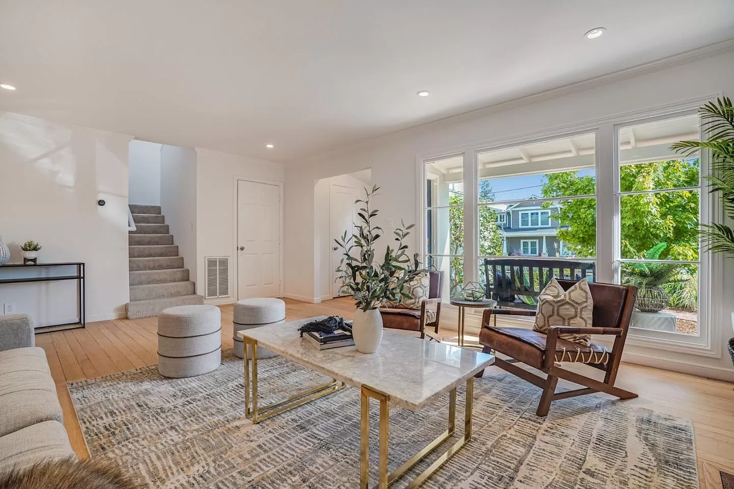 A living room with a marble coffee table , chairs , ottomans and stairs.