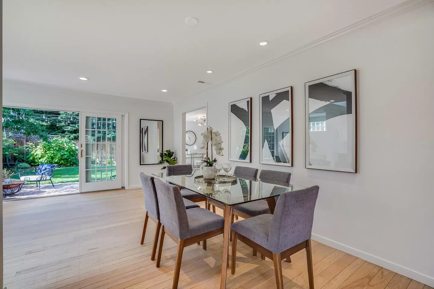 A dining room with a glass table and chairs and paintings on the wall.