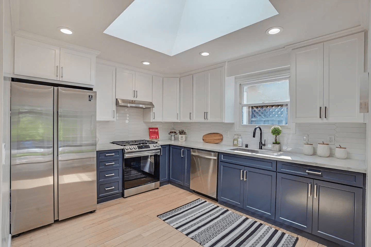 A kitchen with blue cabinets , white cabinets , stainless steel appliances and a skylight.