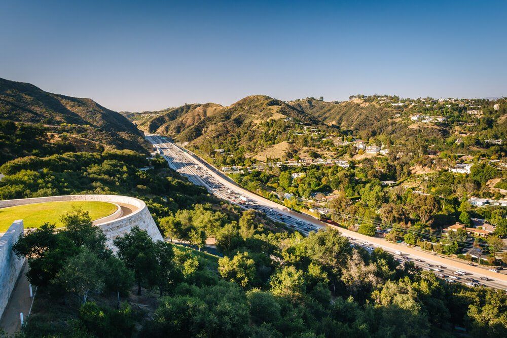 An aerial view of a highway going through a valley surrounded by trees.