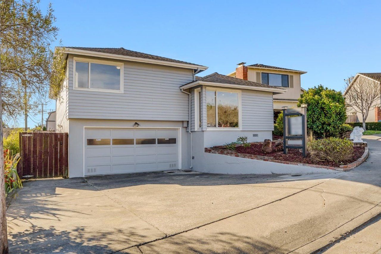 A white house with a garage and a wooden fence is for sale.
