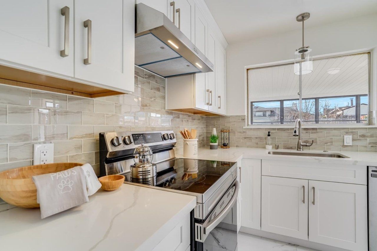 A kitchen with white cabinets , a stove , a sink , and a window.
