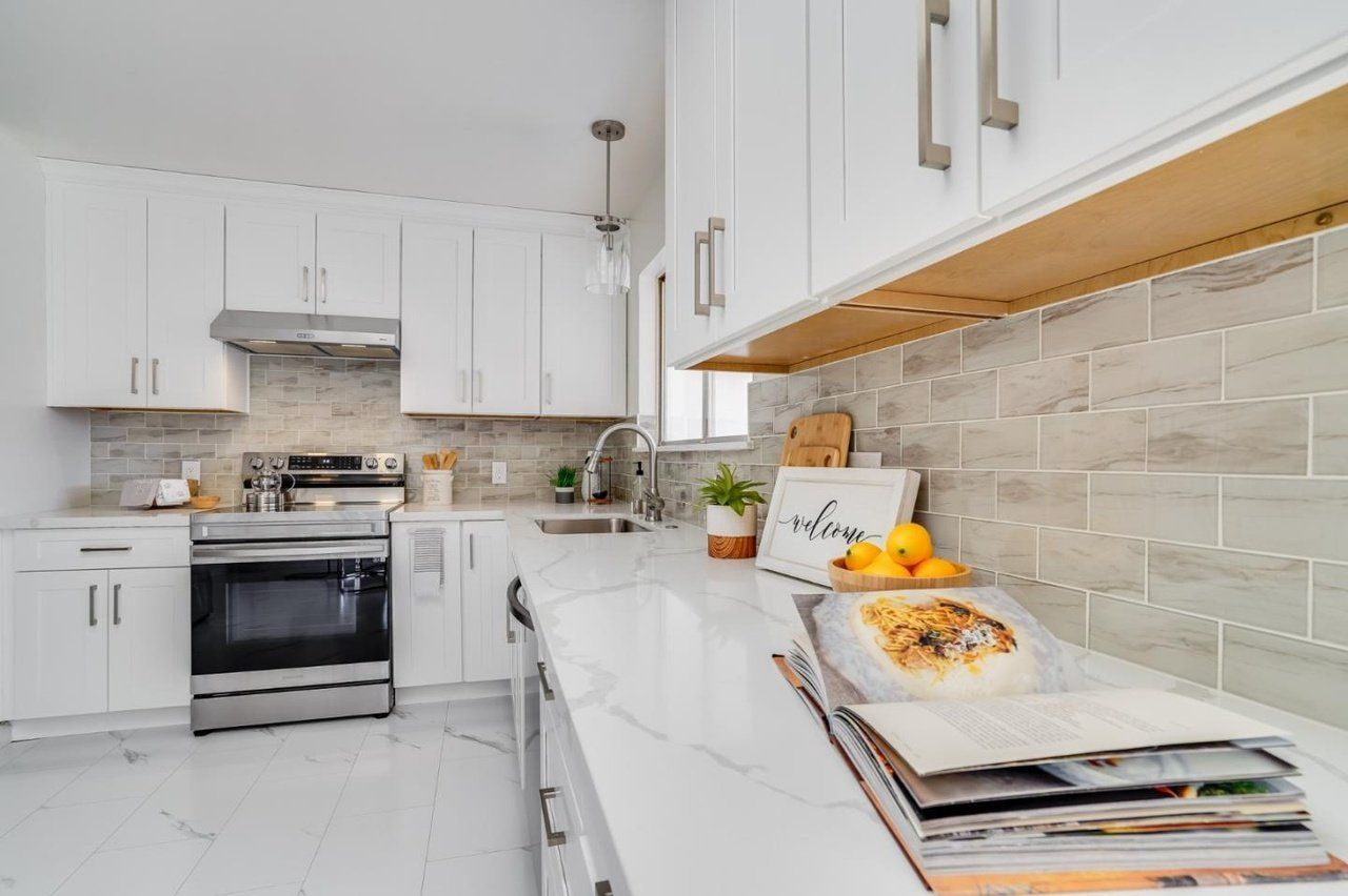 A kitchen with white cabinets , stainless steel appliances , and a stack of magazines on the counter.