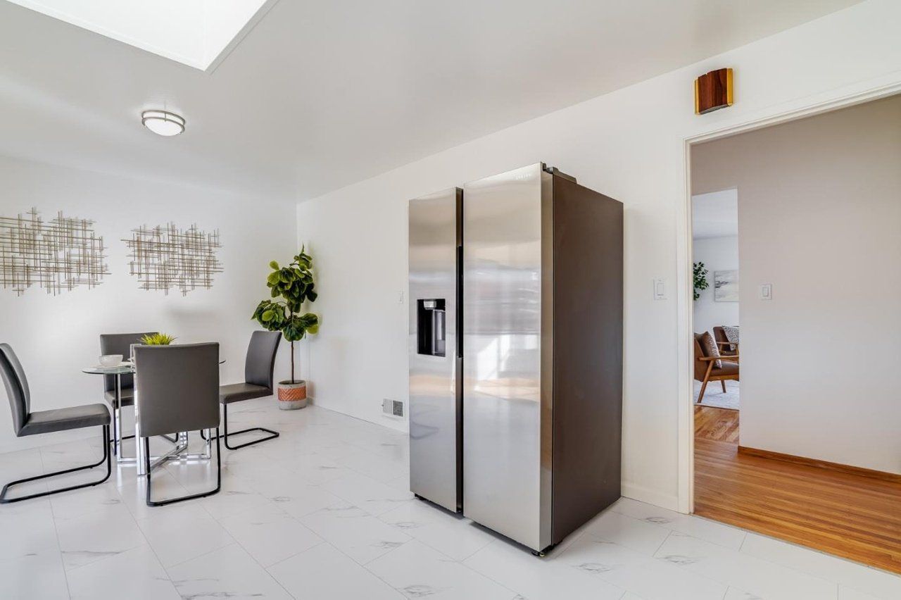 A stainless steel refrigerator is sitting in a dining room next to a table and chairs.