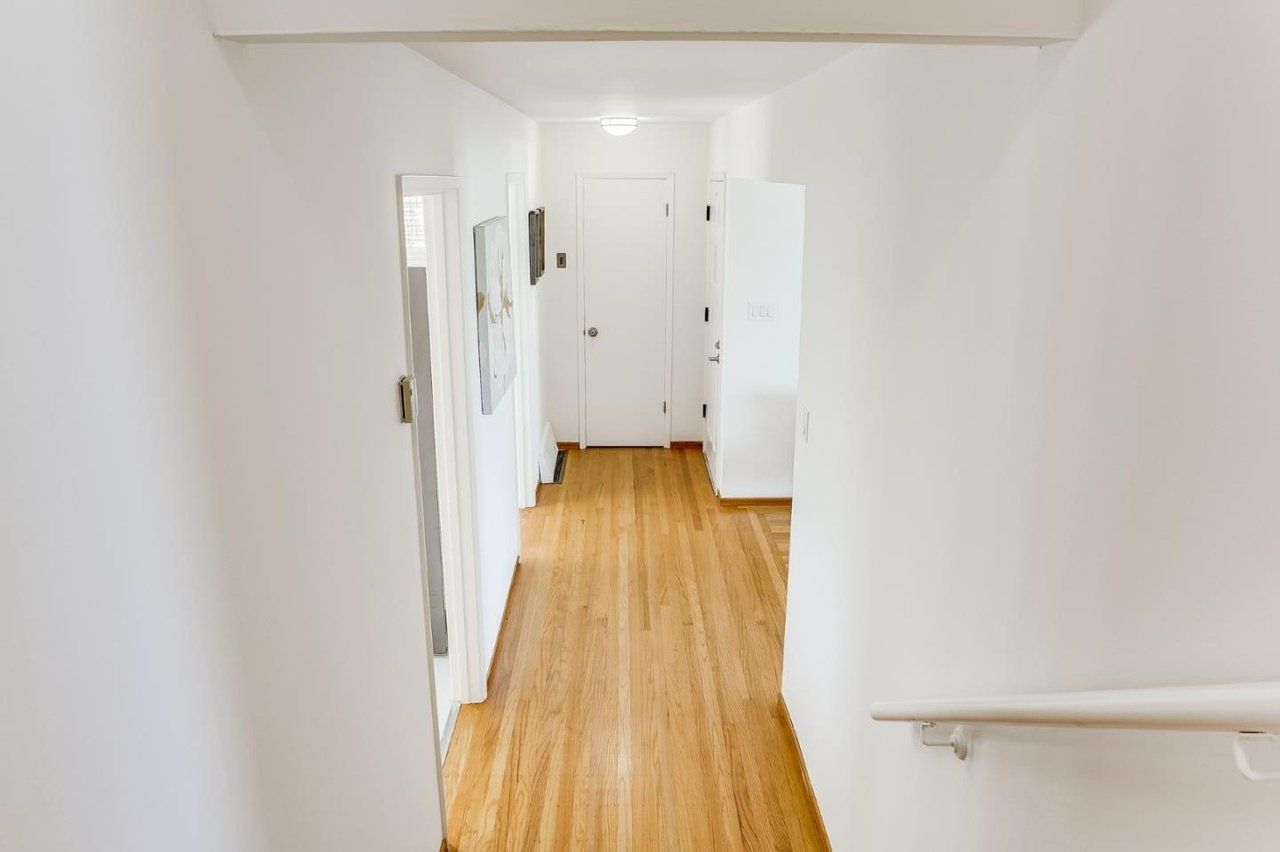 A long hallway with hardwood floors and white walls leading to a door.
