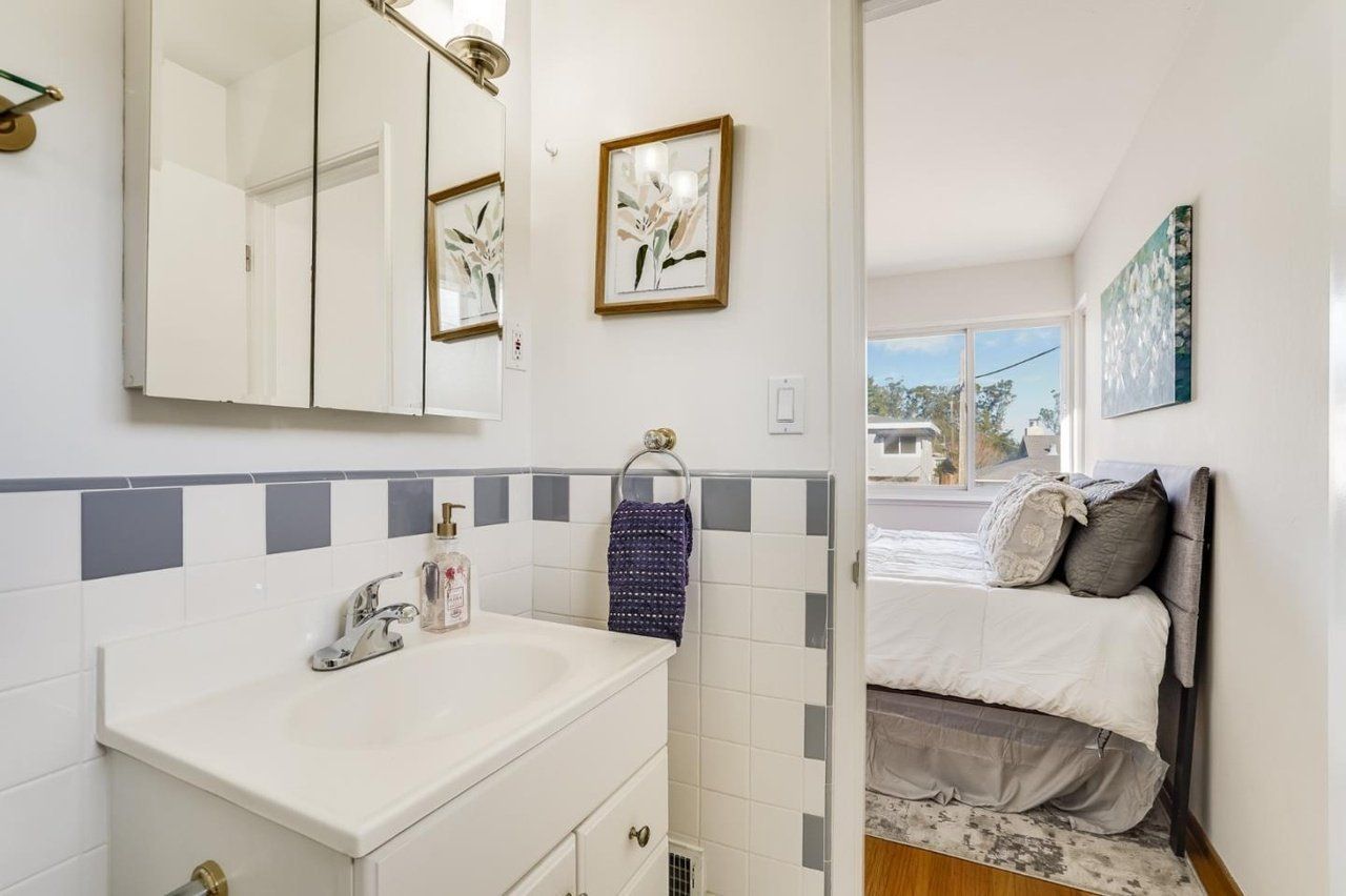 A bathroom with a sink and mirror next to a bedroom.