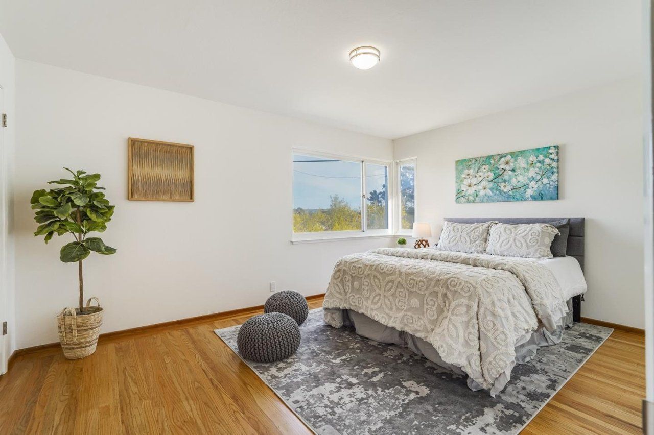A bedroom with a bed , rug , ottomans and a window.