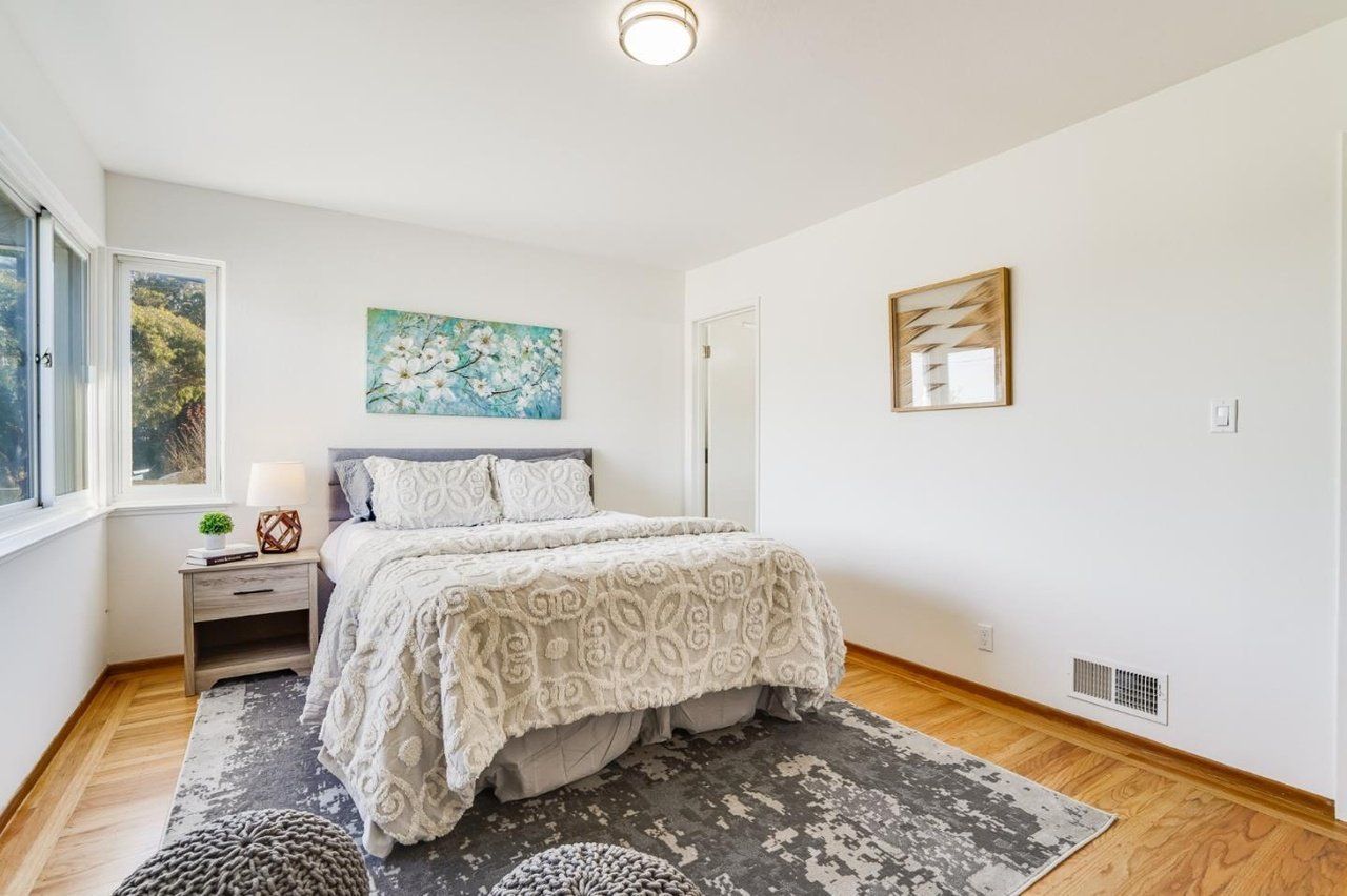 A bedroom with a bed , nightstand , rug and window.