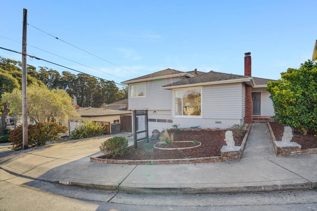 A white house with a brick chimney is on the corner of a street.