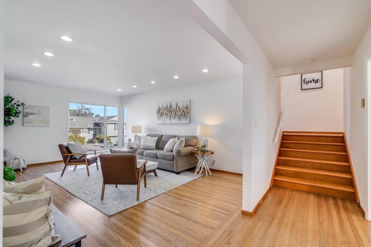 A living room with a couch , chairs , and stairs leading up to the second floor.