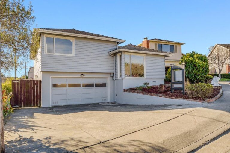 A white house with a garage and a wooden fence is for sale.