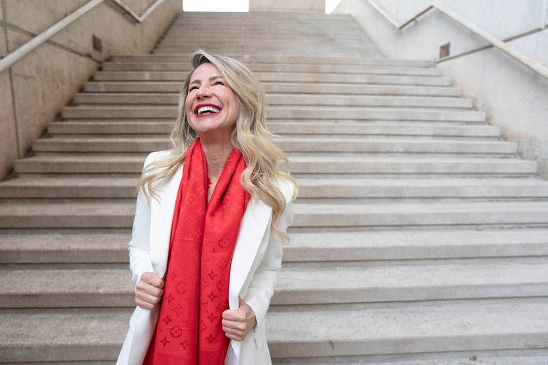 A woman wearing a red scarf and a white jacket is standing on a set of stairs.