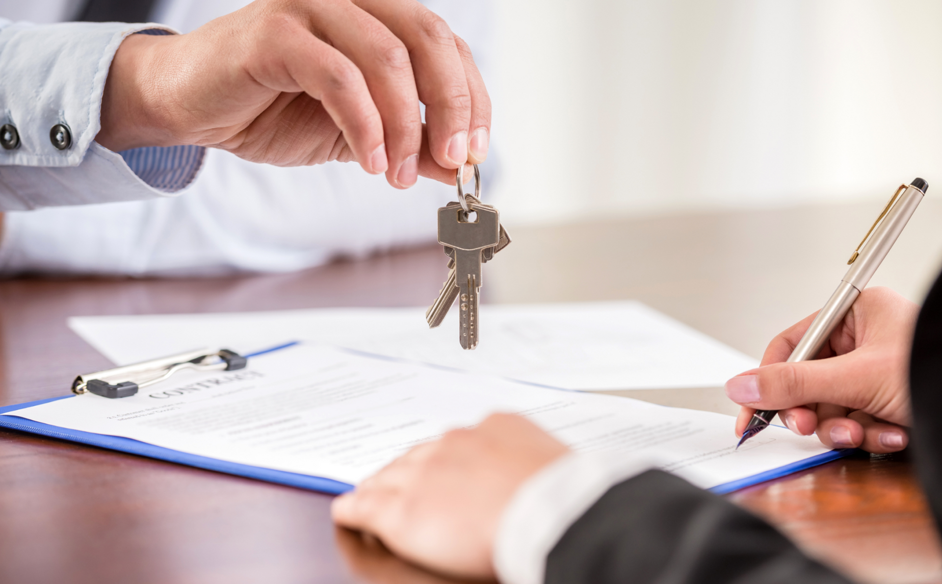 A man is giving a key to a woman who is signing a document.