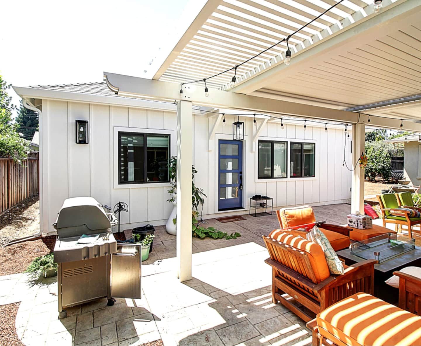 A white house with a patio area with a grill and chairs under a pergola.