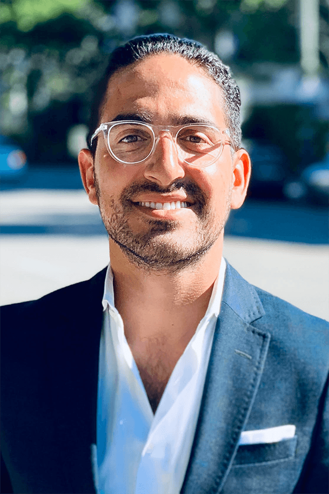 A man wearing glasses and a suit is smiling for the camera.