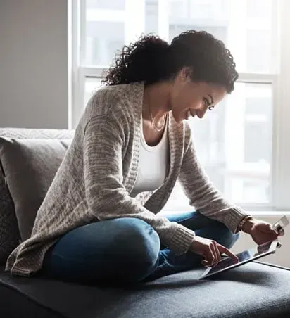 A woman is sitting on a couch using a tablet computer.