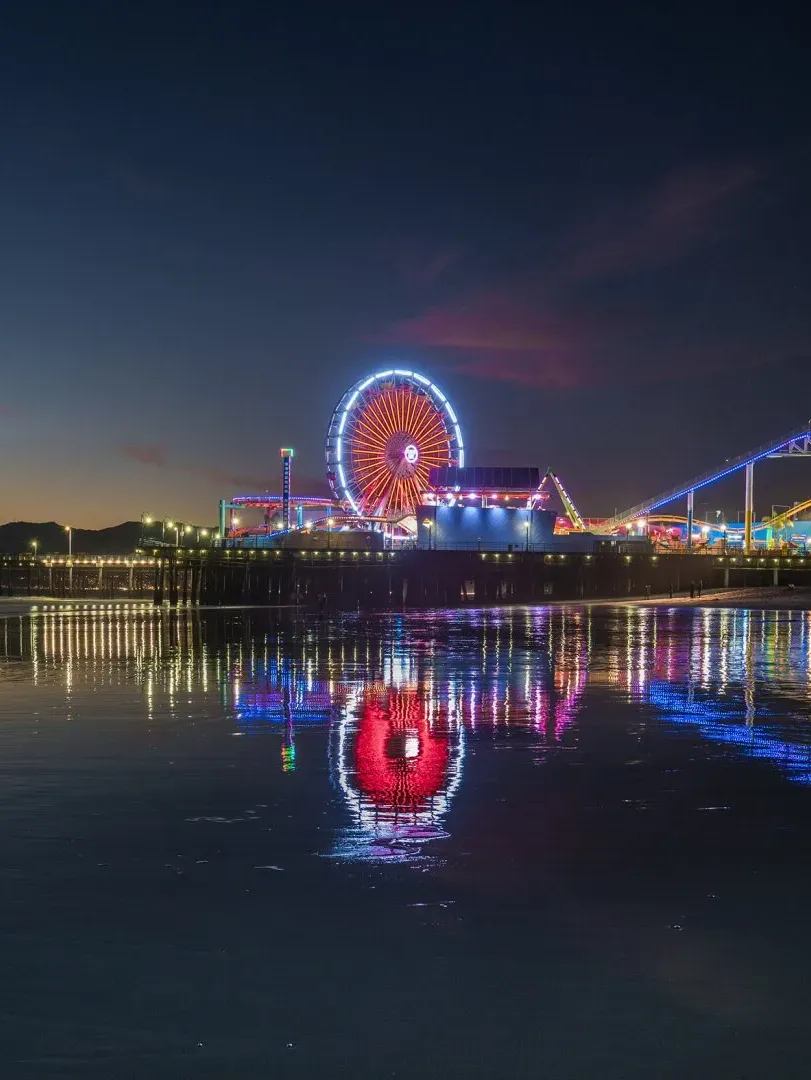 A ferris wheel is reflected in the water at night.