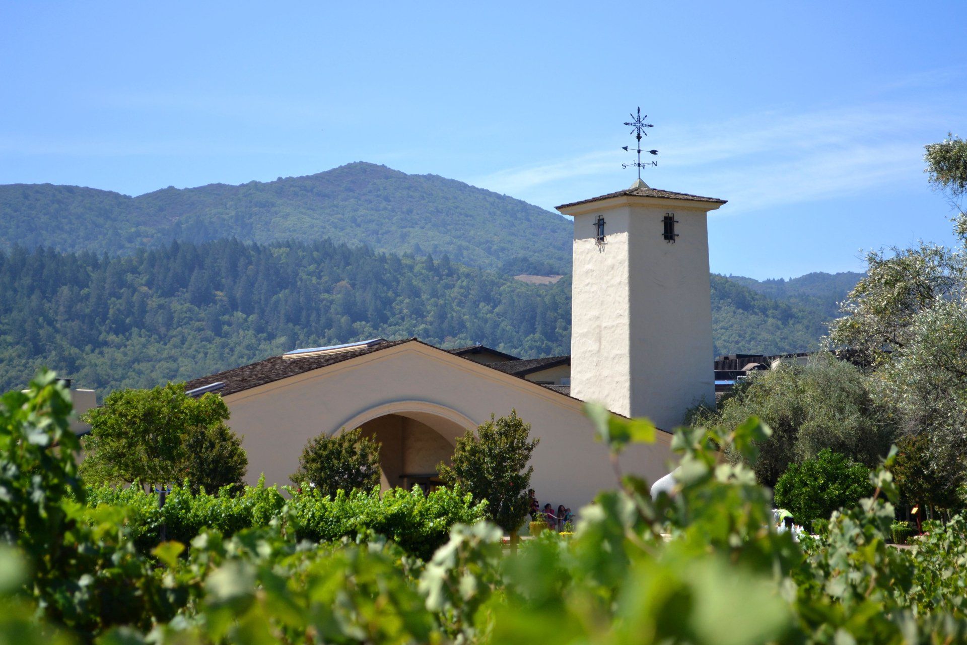 A church with a cross on top of it is surrounded by trees and mountains.