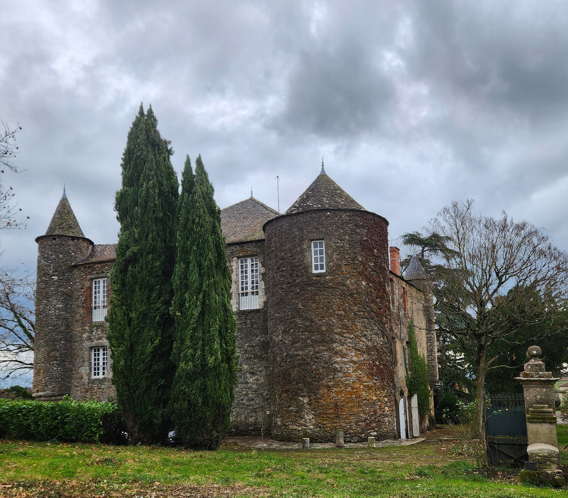Stone castle with turrets under a cloudy sky, tall trees in the foreground.