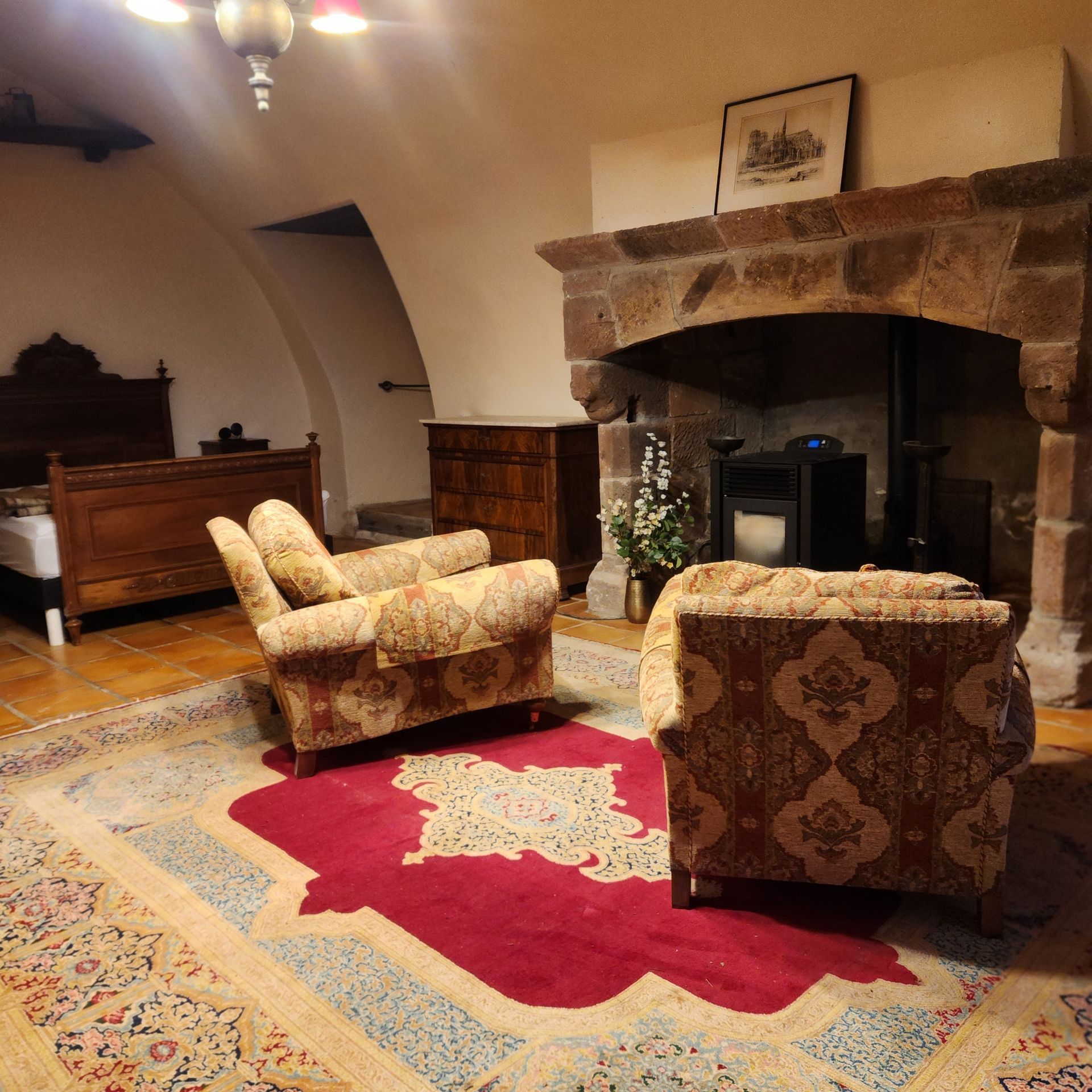 Chambre chaleureuse meublée d'antiquités. Deux fauteuils à motifs font face à une cheminée en pierre. 