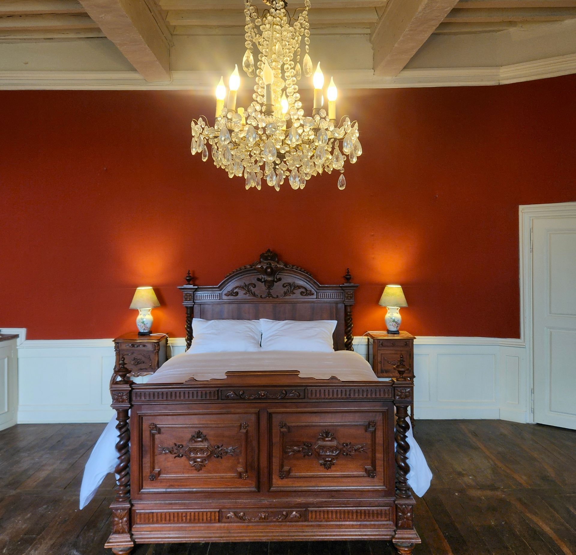 Chambre avec lit en bois orné, mur rouge, lustre et lampes de chevet.