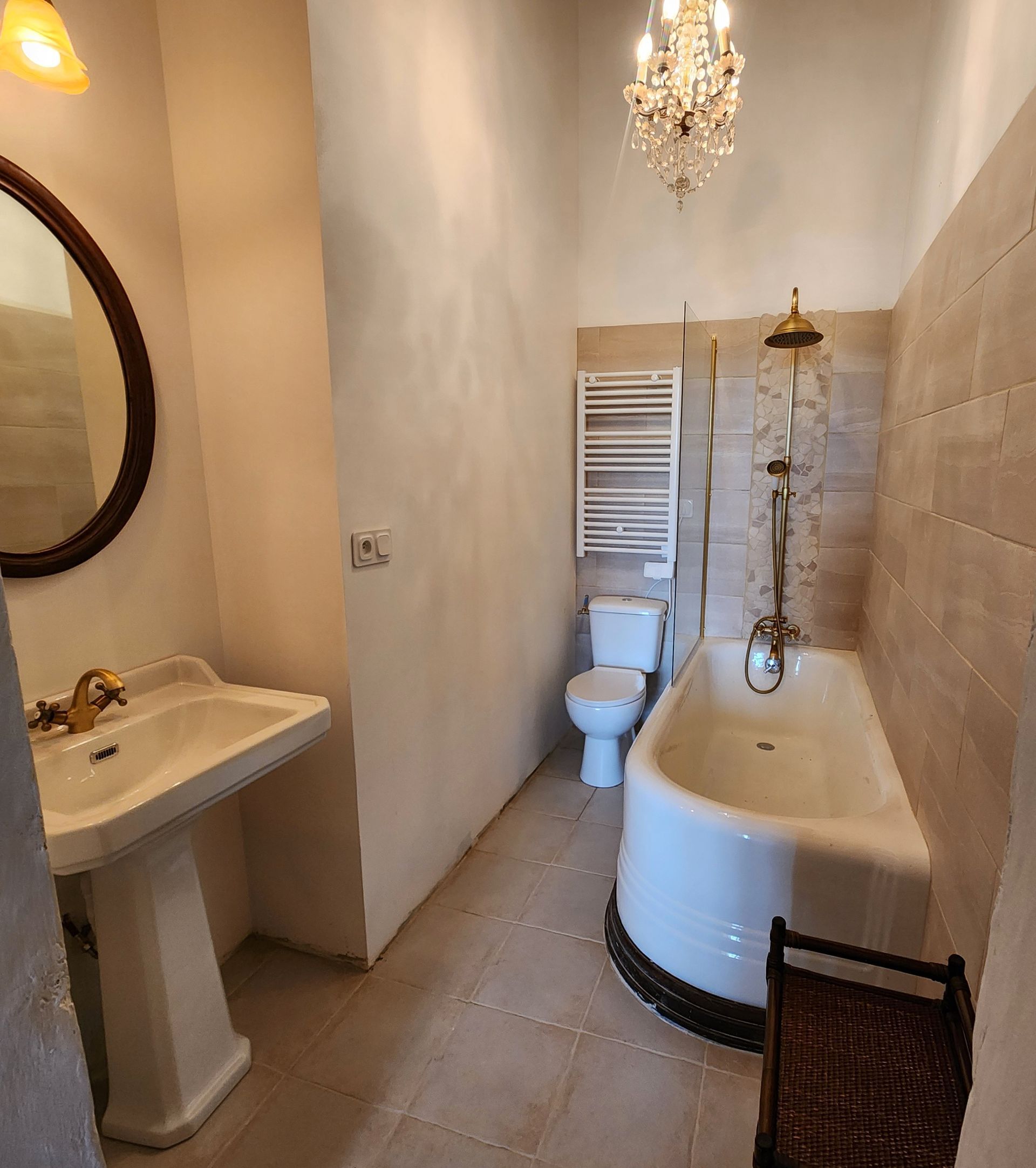 Salle de bains avec lavabo sur pied blanc, toilettes, baignoire et petit lustre.