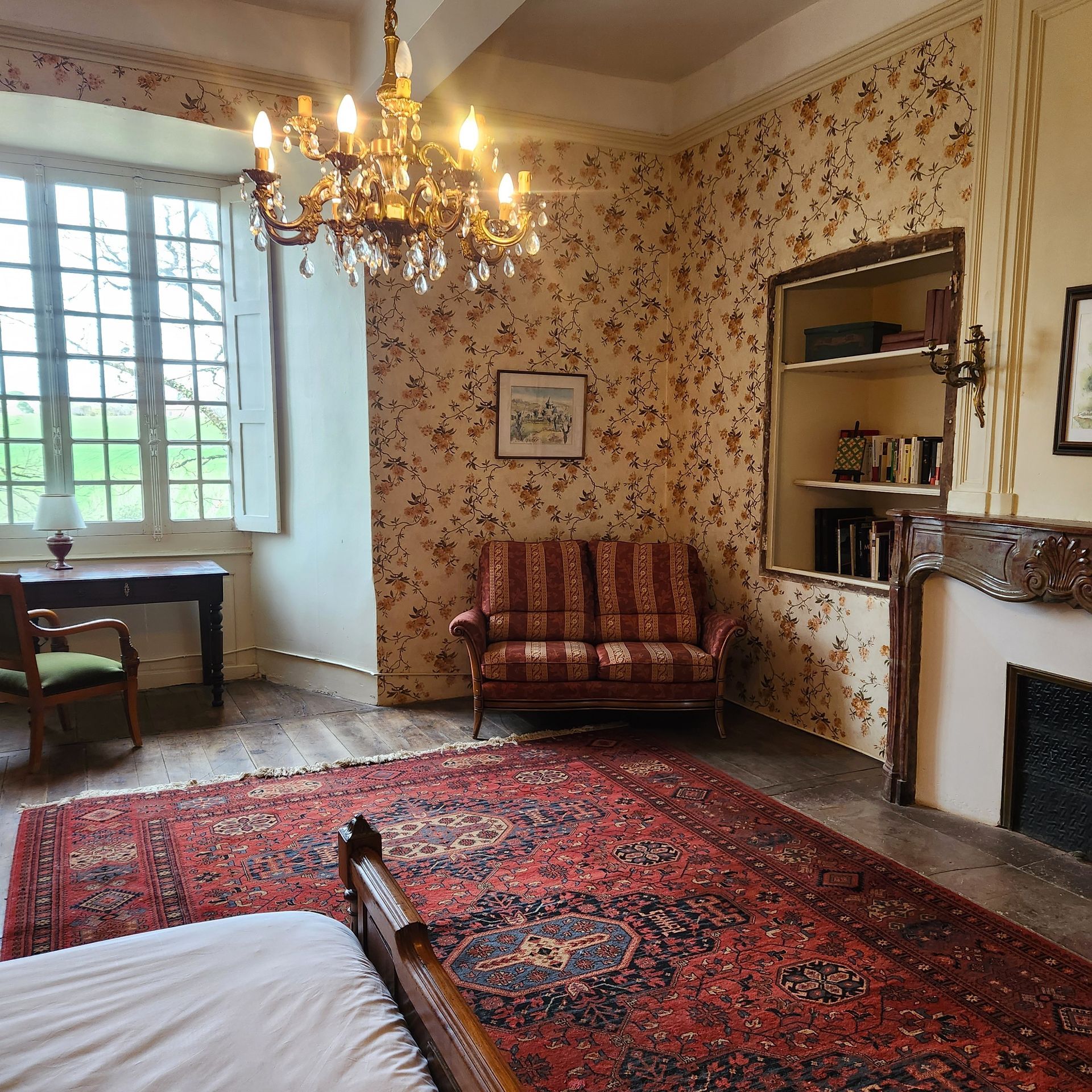 Une chambre classique avec une causeuse rayée, un lustre et un coin cheminée.