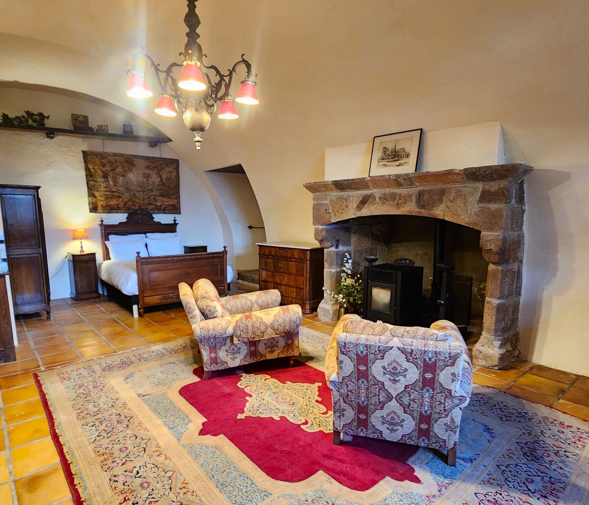 Chambre chaleureuse meublée d'antiquités. Deux fauteuils à motifs font face à une cheminée en pierre. 
