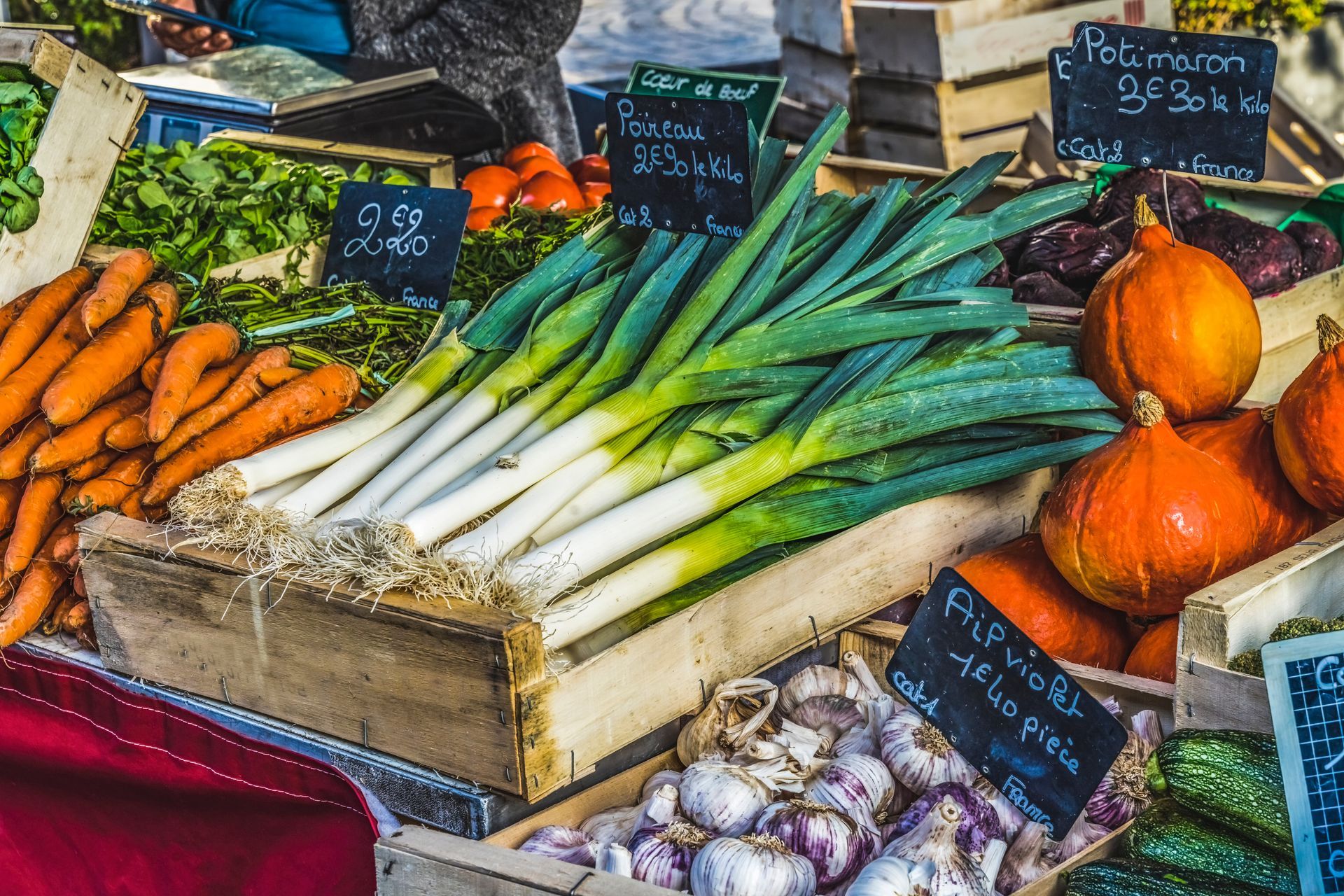Vegetable market stall with carrots, leeks, pumpkins, garlic, and other produce.