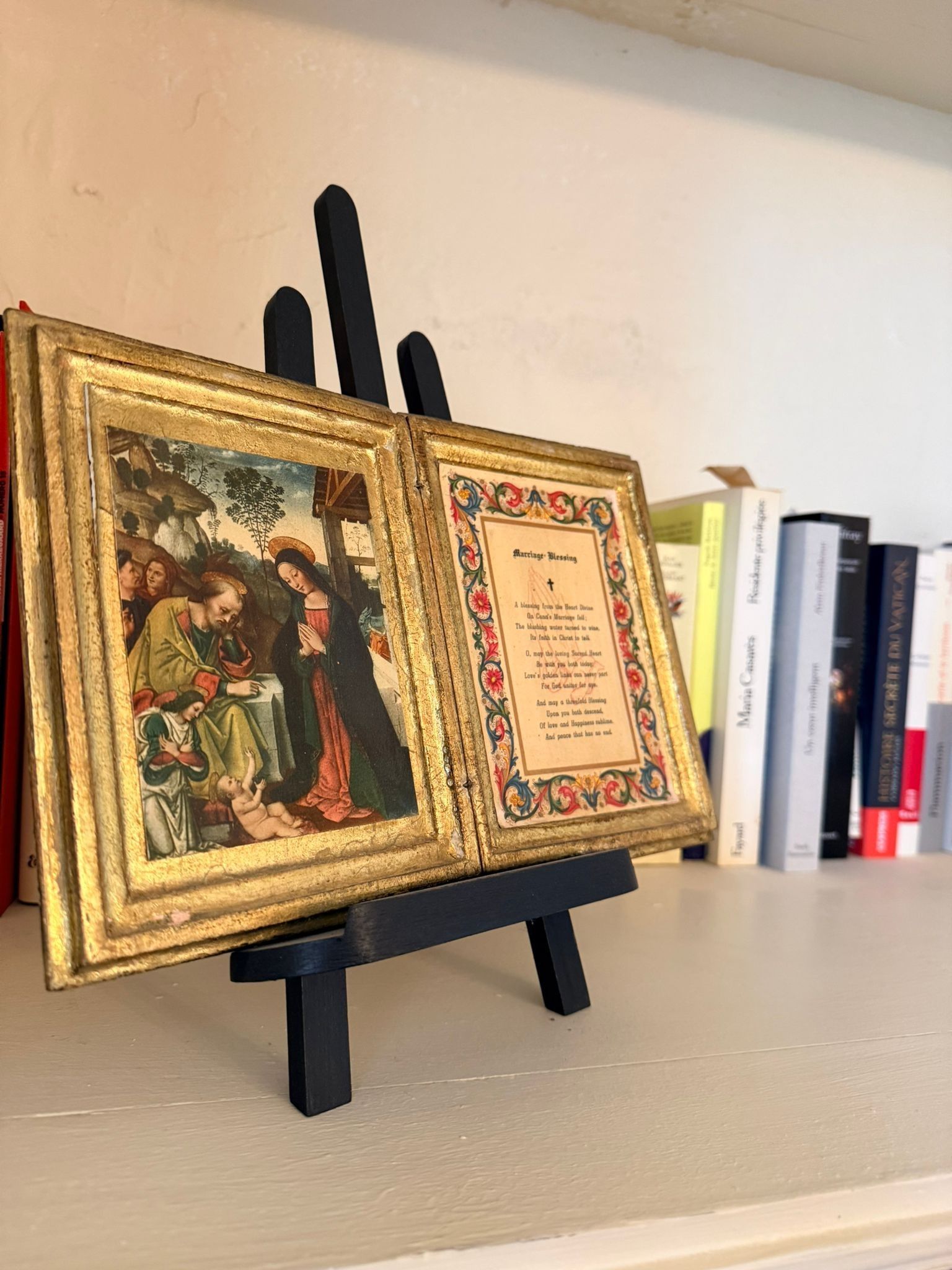 Un diptyque encadré présentant de l'art religieux et un texte sur un chevalet, exposé devant une étagère de livres.