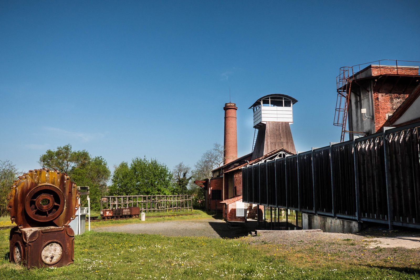 Abandoned industrial site with a brick chimney and rusted machinery on a sunny day.