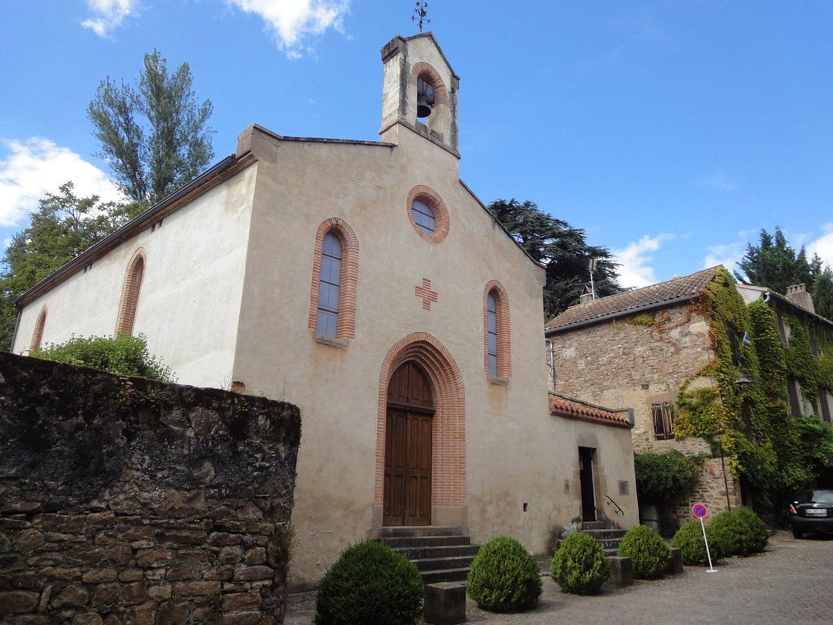 Church building with arched doorway and bell tower, stone wall in front, blue sky.