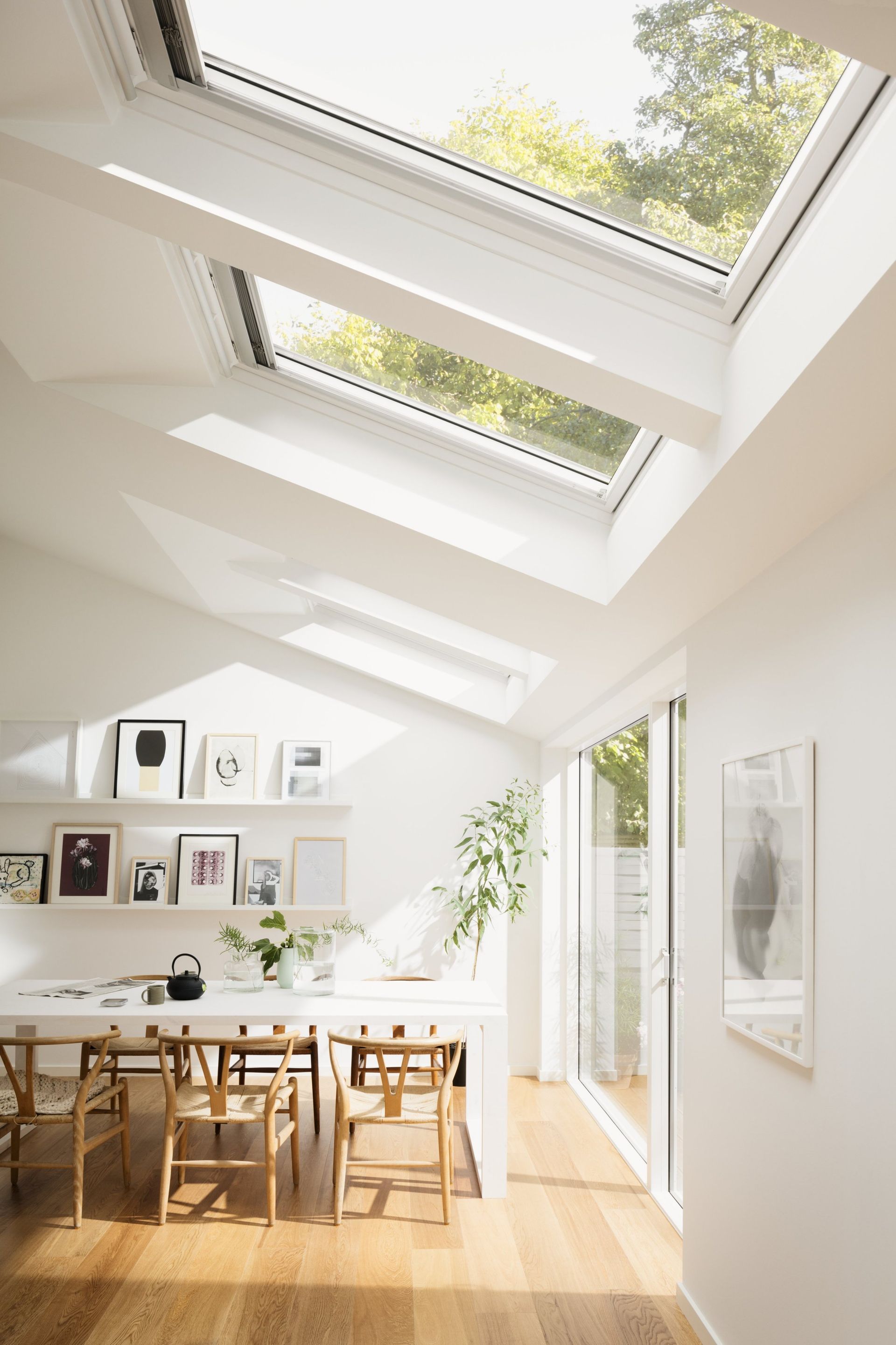 Bright white dining room with skylights and wooden floors, table with chairs, and framed art.