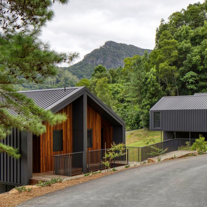 Two modern cabins with dark exteriors and wood paneling in a mountain setting.