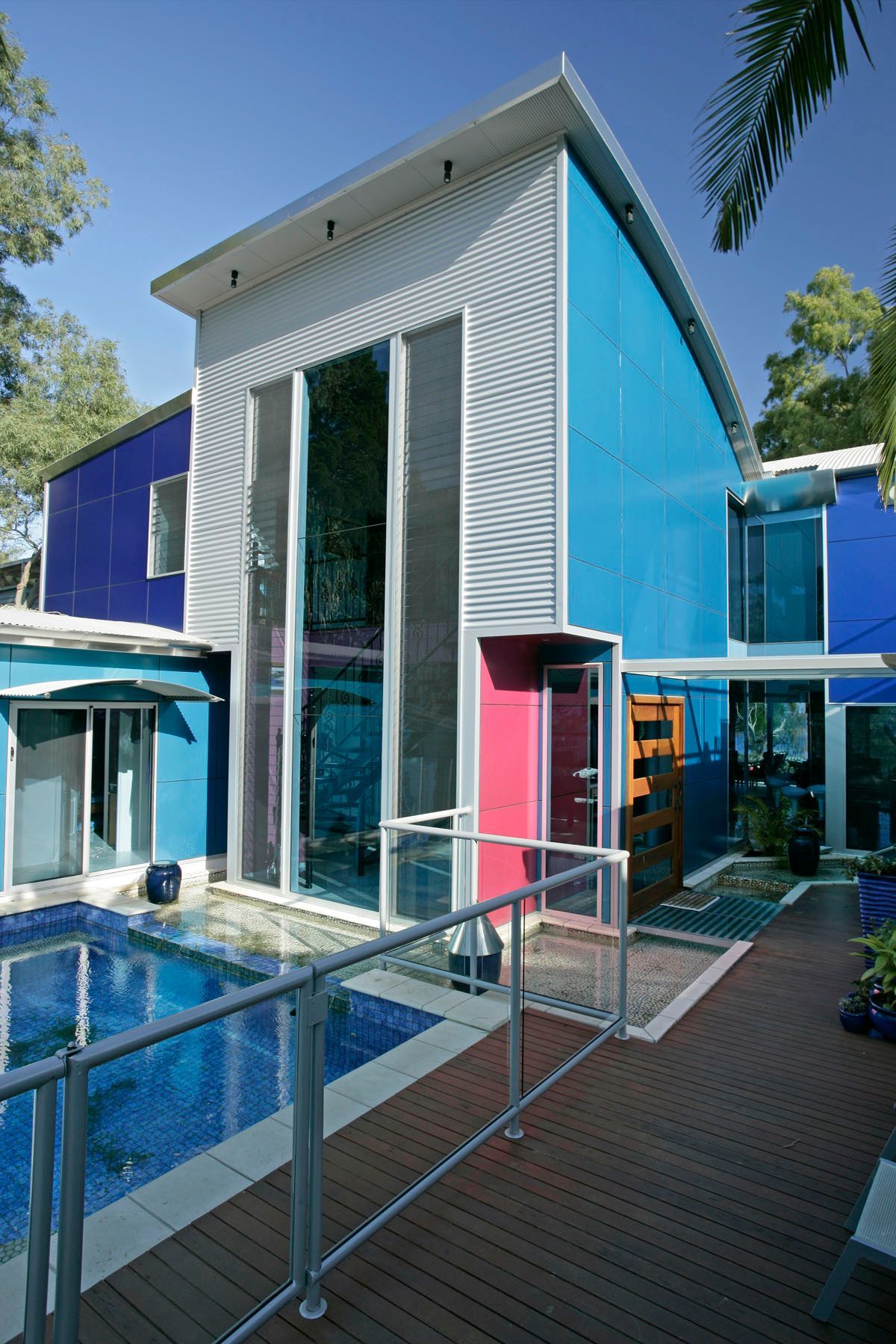Modern house with blue and pink accents, pool, and wooden deck.
