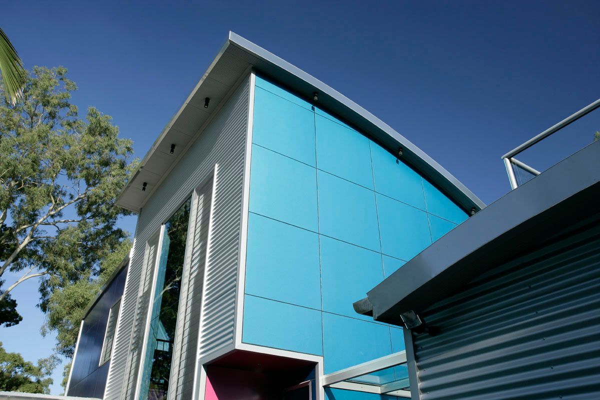 Modern building with a curved, teal-blue facade and corrugated metal siding against a blue sky.