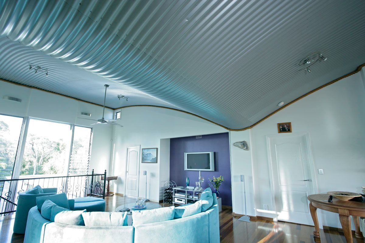 Interior living room with wavy, corrugated metal ceiling. Blue sofa, white walls, purple accent wall.