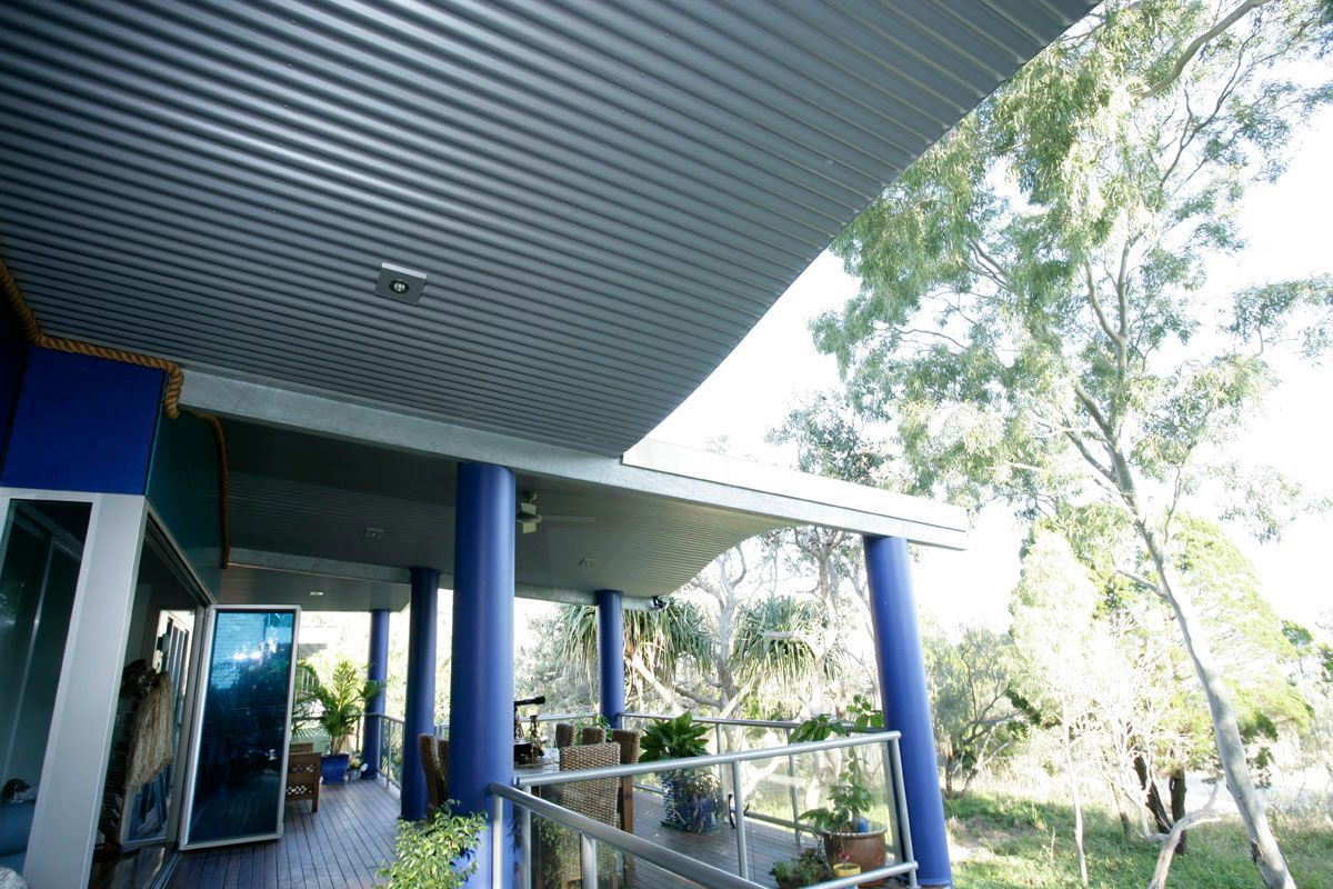 Blue-columned veranda with corrugated metal roof overlooking a lush tree-filled landscape.