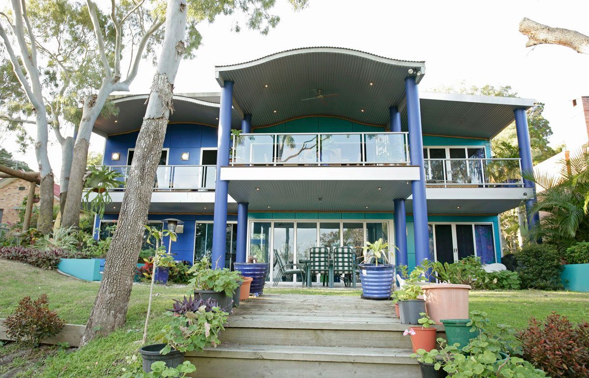 Two-story blue house with teal accents, balcony, overlooking a grassy yard and stairs.