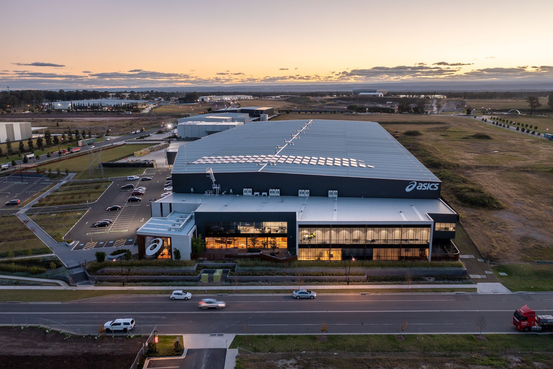 ASICS distribution center exterior at dusk, modern design, cars on road in foreground.