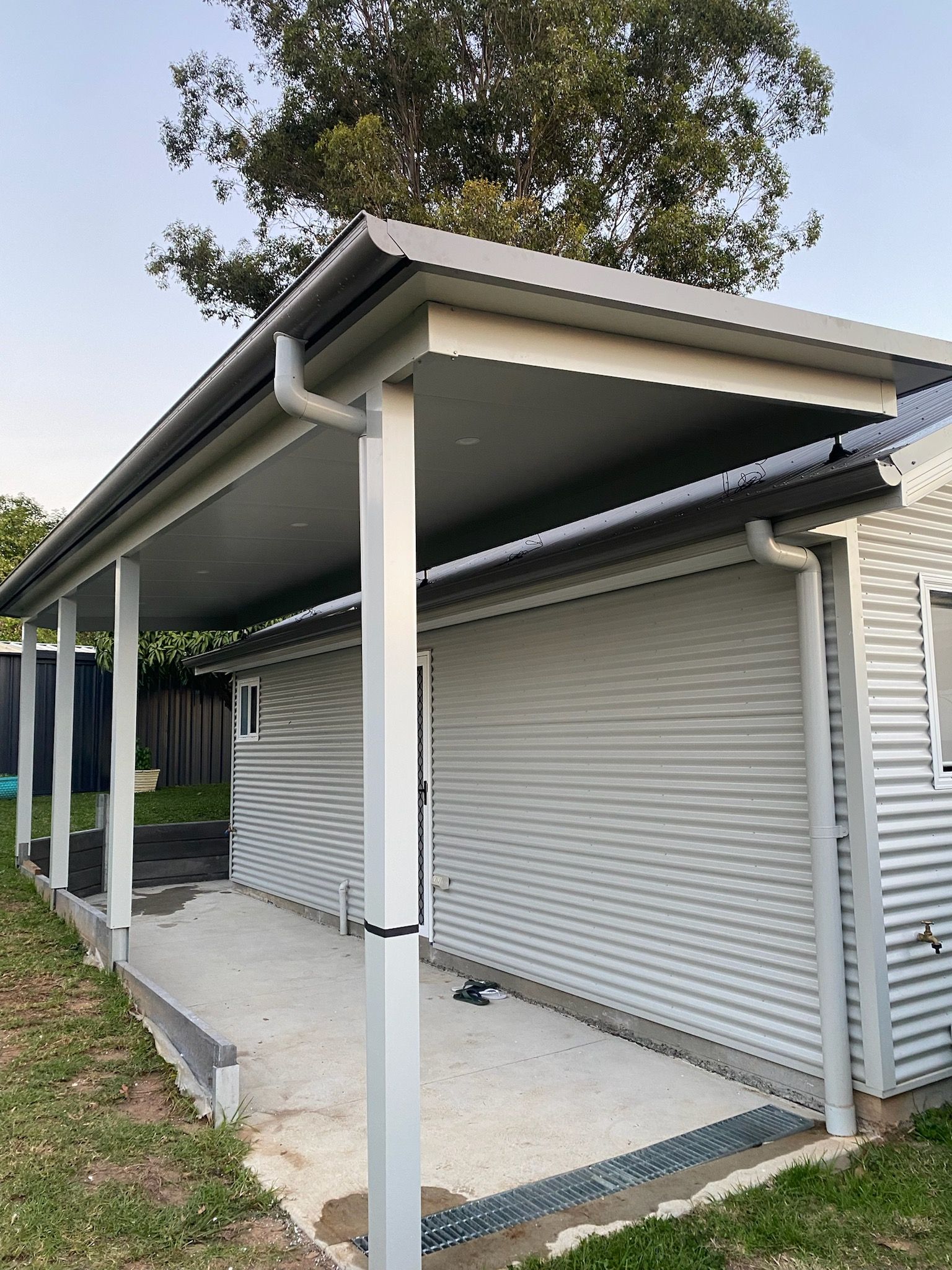 Gray corrugated iron shed with a matching corrugated iron roof and guttering, next to a cement patio.