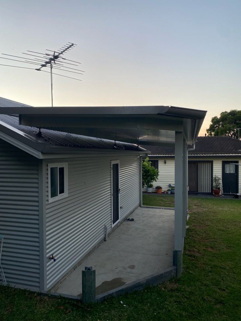 A building with a covered patio, antenna, and a grassy lawn in the late afternoon.