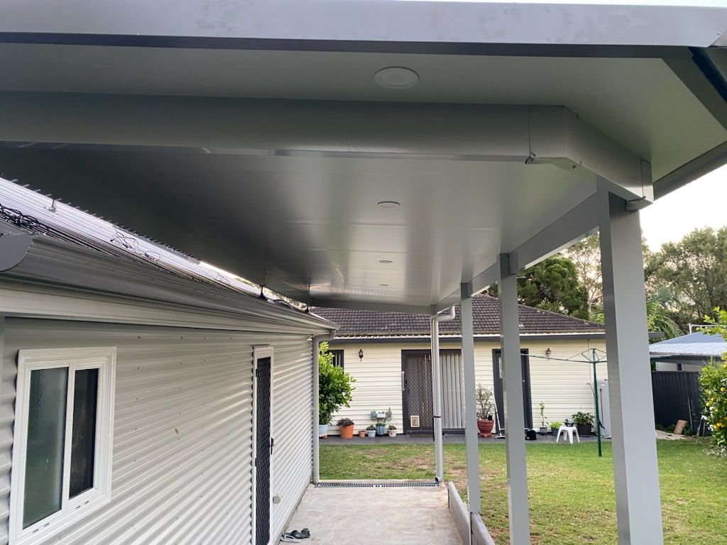 Gray covered patio, next to a white house, overlooking a backyard with other homes and green grass.