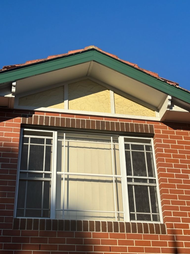 Brick building with a white-framed window, a decorative triangular roof section.
